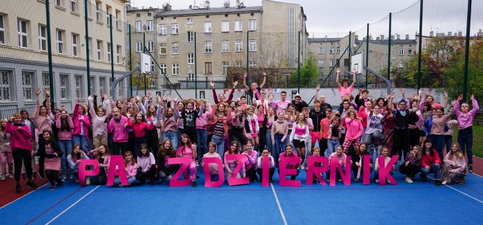 Uczniowie XIII LO ubrani na różowo podczas wspólnego zdjęcia na boisku szkolnym.